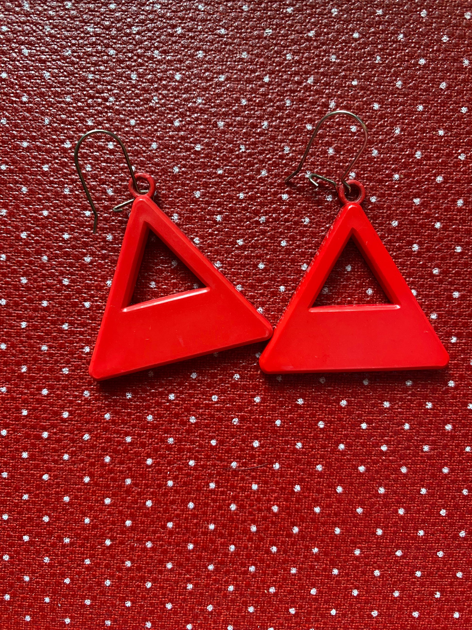 Red 80s triangle-shaped earrings on a red textured background with white polka dots